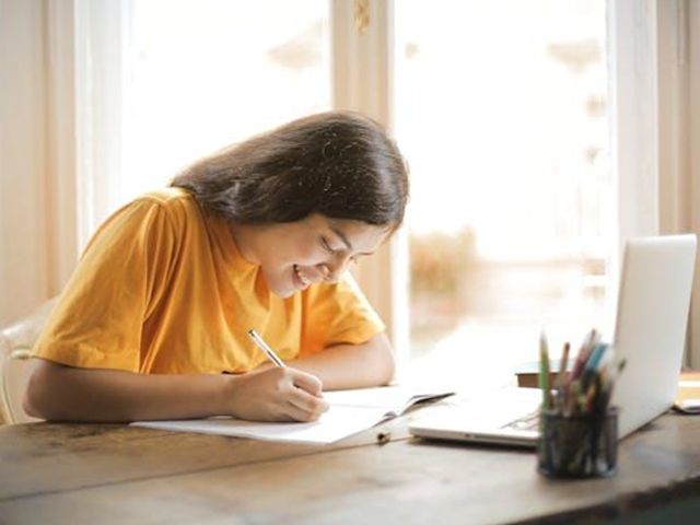 A girl in a yellow shirt writing in her notebook